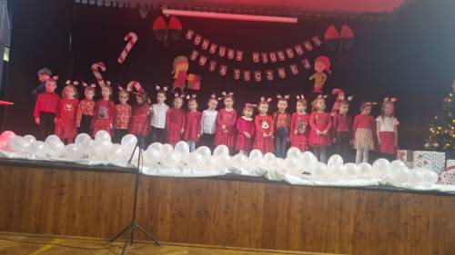 Dzieci na scenie w odświętnych strojach śpiewające piosenki